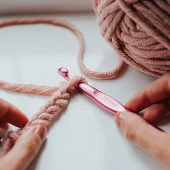 Mains de femme qui manipulent un crochet et une pelote pour faire des noeuds